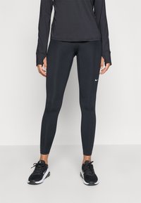 Colanți negri Nike dintr-un material neted, elastic, cu un design ajustat, asortați cu pantofi sport negri, având un logo alb pe coapsa stângă.