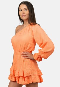 Eén-schouder, feloranje jurk van textuurstof, lange puff-mouw, cinched taille en ruches aan de zoom.