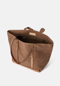 Bruine canvas tas met een gestructureerde bronzen bodem, dubbele handvatten en een open interieur met een ritszak en een merketiket.