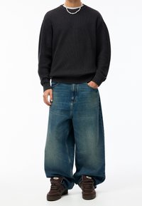 Suéter negro de canalé con mangas largas, combinado con jeans de denim de talle alto y de gran tamaño en un tono azul claro. Zapatillas marrones completan el atuendo.