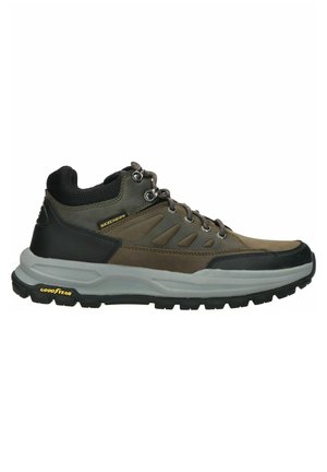 Zapato de senderismo marrón con acentos grises, parte superior de malla, talón de goma negro y cordones circulares. Presenta la marca "SKECHERS" y "GOODYEAR" en la suela.