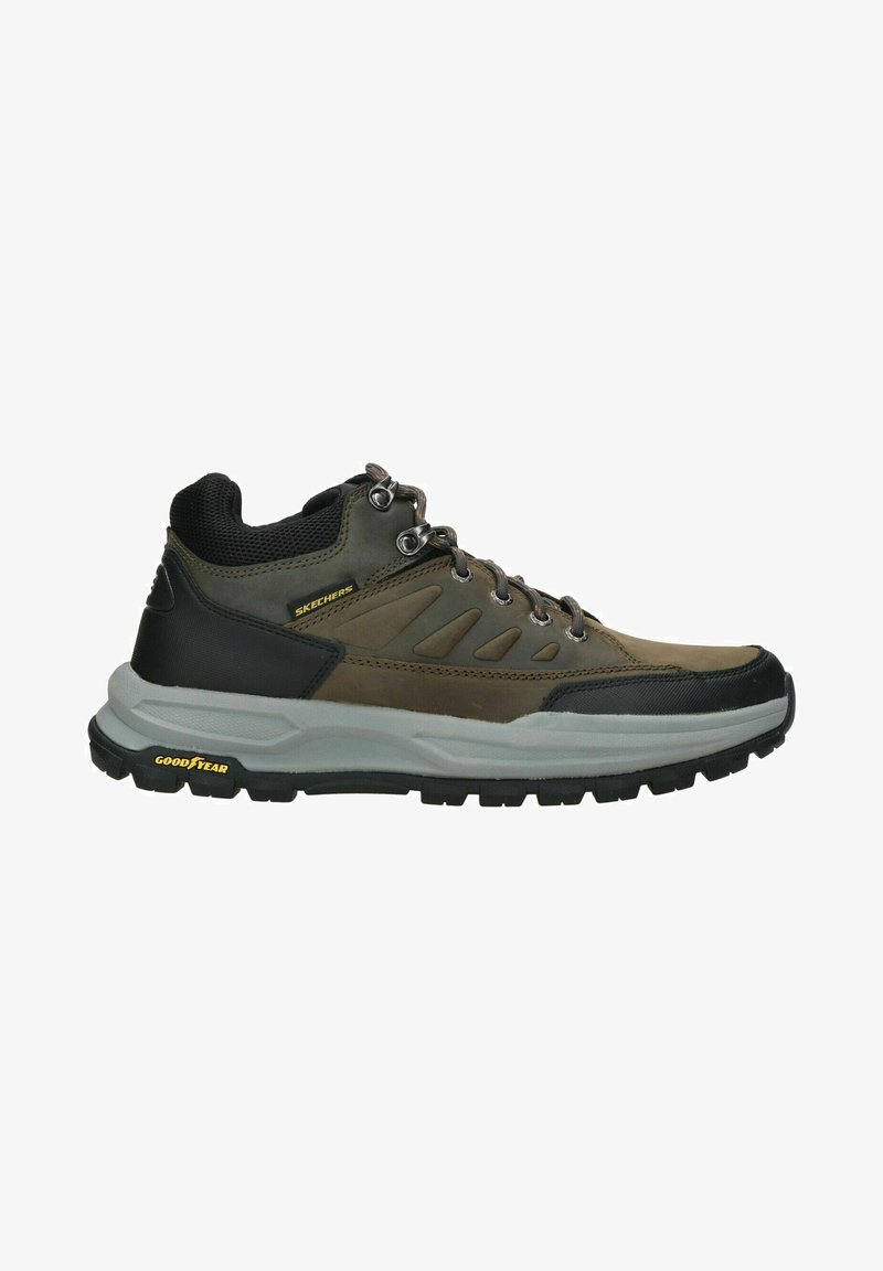 Zapato de senderismo marrón con acentos grises, parte superior de malla, talón de goma negro y cordones circulares. Presenta la marca "SKECHERS" y "GOODYEAR" en la suela.