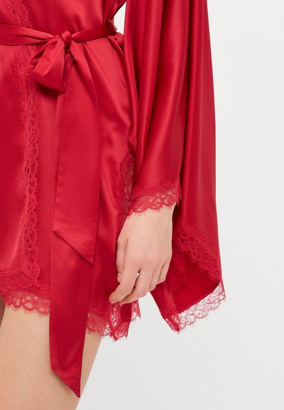 Accappatoio in raso rosso con bordo in pizzo alle maniche e all'orlo, completo di una cintura coordinata. Il tessuto ha una texture liscia e una leggera lucentezza.