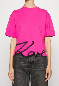Fuchsia Baumwoll-T-Shirt mit Oversize-Passform, rundem Hals und schwarzem gesticktem "Love"-Detail am Saum. Kurze Ärmel und weicher Stoff.