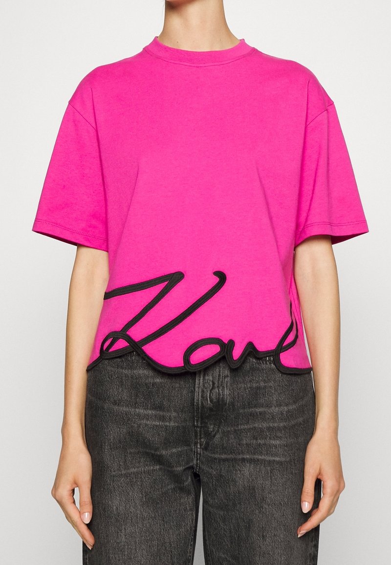 Fuchsia Baumwoll-T-Shirt mit Oversize-Passform, rundem Hals und schwarzem gesticktem "Love"-Detail am Saum. Kurze Ärmel und weicher Stoff.
