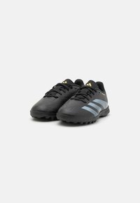 Baskets de sport noires avec une surface texturée, dotées de trois rayures bleu clair et d'accents dorés, conçues pour une utilisation sur gazon.