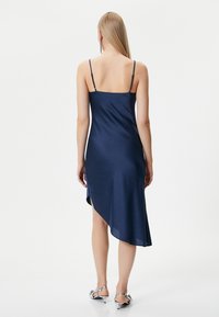 Marineblaues Satin-Kleid mit verstellbaren Spaghettiträgern, asymmetrischem Saum und seitlicher Schlitz, das eine glatte Textur und eine elegante Silhouette zeigt.