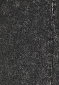 Tela de mezclilla negra con una textura desgastada, que muestra variaciones de tonos claros y oscuros. Presenta costuras estándar a lo largo de las costuras.