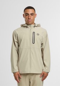 Světle béžová nepromokavá bunda s kapucí, předním zipem, náprsní kapsou a logem na hrudi, s jemnou texturou.