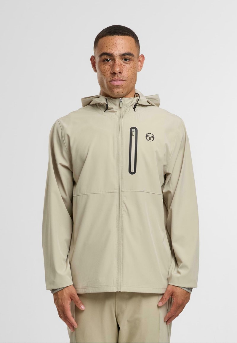 Světle béžová nepromokavá bunda s kapucí, předním zipem, náprsní kapsou a logem na hrudi, s jemnou texturou.