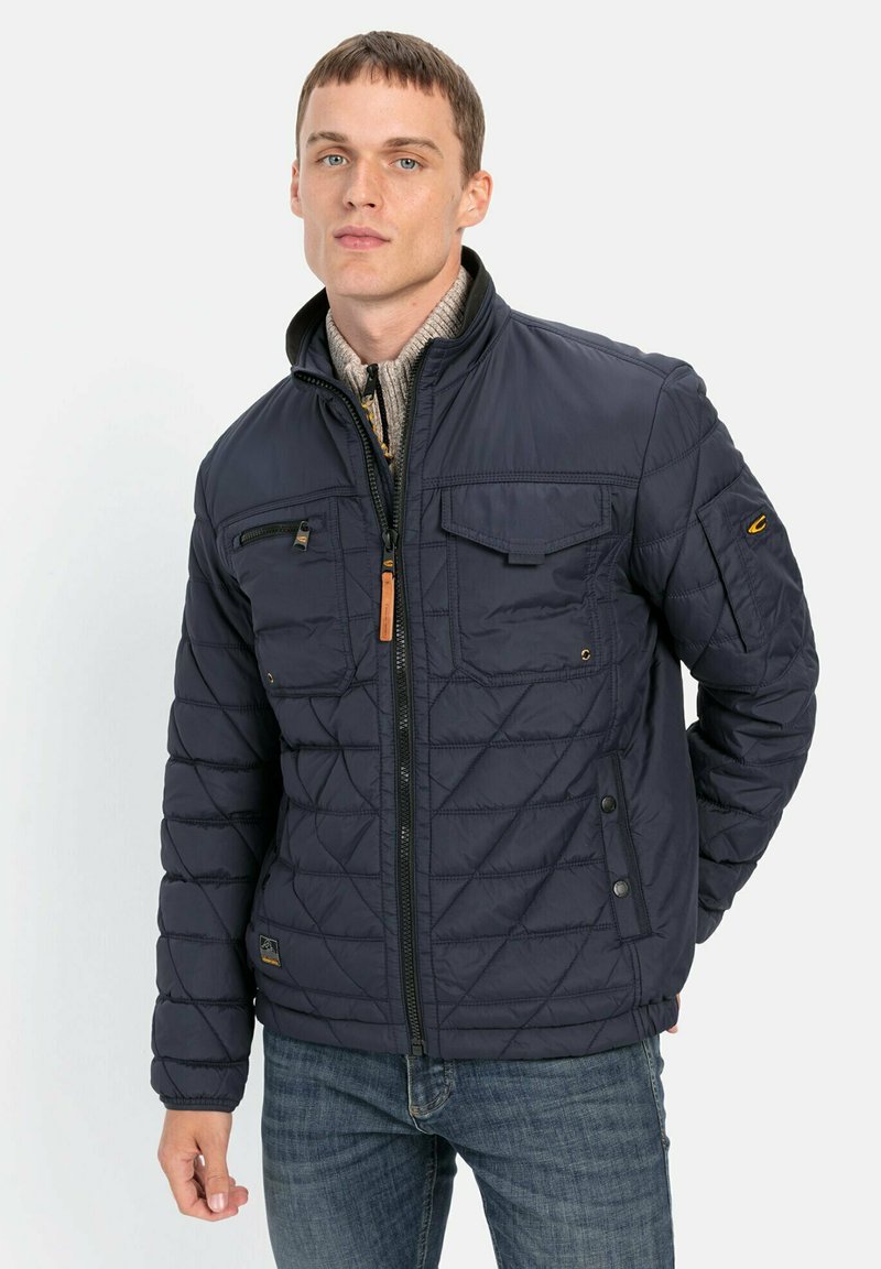 Mørkeblå quiltet jakke med lynlås foran, to brystlommer og struktureret krave. Med toggle og logo detaljer. Glat stoftekstur.