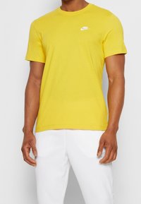 Yellow cotton t-shirt with short sleeves, crew neck, and small white Nike logo on the chest. Smooth texture, casual fit.