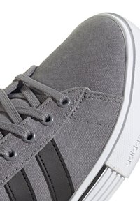 Gray canvas sneaker with black stripes, textured surface, and round eyelets. White rubber sole with a patterned edge.