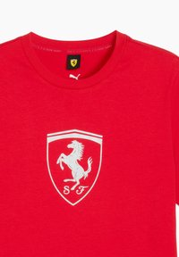 Rød t-shirt med et hvidt Ferrari-logo med en oprejst hest inde i en skjoldform. Mærket viser "SCUDERIA FERRARI" og et Puma-logo.