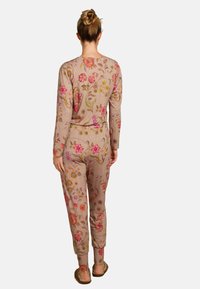 Floral-patterned jumpsuit in beige fabric featuring long sleeves and an elastic waistband, with colorful embroidered flowers and leaves.