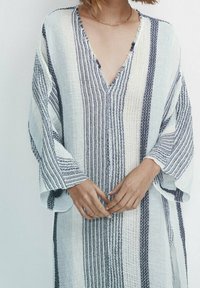 Tunique légère à rayures avec un col en V profond. Confectionnée dans un tissu texturé aux motifs bleus et blancs, manches larges et coupe décontractée.