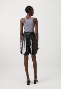 Un haut sans manches gris associé à un short noir en sequins, avec une taille élastique et une texture brillante, porté avec des sandales à talons carrés.