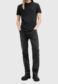 T-shirt in cotone nero con un piccolo logo sul petto, abbinato a jeans in denim grigio scuro e stivali neri chunky. Design semplice e aderente.