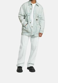 Ljusblå denimjacka med två bröstfickor och två sidfickor,  i kombination med vita, löst sittande byxor och svarta sneakers.