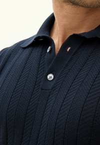 Mörkblå polo skjorta med en strukturerad, ribbad design. Kort krage, två knappar och en liten håldetalj nära kragen.