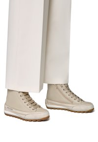 Zapatillas altas beige de cuero con un acento de ante texturizado, suela de goma y cordones tonales; combinadas con pantalones anchos blancos.