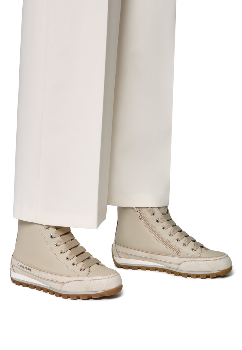Zapatillas altas beige de cuero con un acento de ante texturizado, suela de goma y cordones tonales; combinadas con pantalones anchos blancos.
