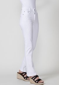 Baltas džinsi ar ziedu izšuvumiem sānos, ar taisnu griezumu un augstu jostasvietu. Apvienoti ar melniem daudzsiksnu platformas sandaliem.