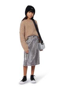 Suéter marrón de punto, falda plateada con lentejuelas, zapatillas negras, gorro negro y un pequeño bolso de hombro metálico con correa.