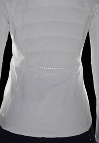 T-shirt sportif blanc à manches longues avec des panneaux texturés, présentant un design incurvé et de petits points réfléchissants le long de la couture arrière. Tissu doux.