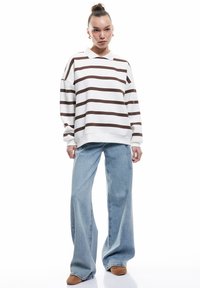 Polo shirt oversized a righe marroni e bianche con maniche lunghe, abbinato a jeans a gamba larga blu chiaro e mocassini marroni.