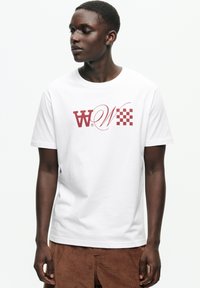 T-shirt alb din bumbac cu un grafic bordo care prezintă litere stilizate "W" și un model cu tablă de șah pe partea stângă.