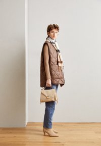 Rude brun vest, beige tørklæde med striber, ribbet sweater, blå jeans, beige håndtaske med guldfinish og beige højhælede støvler.