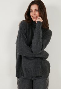 Charcoalgrijze oversized trui met een opstaande kraag, ribgebreide manchetten en zoom, met een zachte textuur en een ontspannen pasvorm. Geschikt voor lagen.
