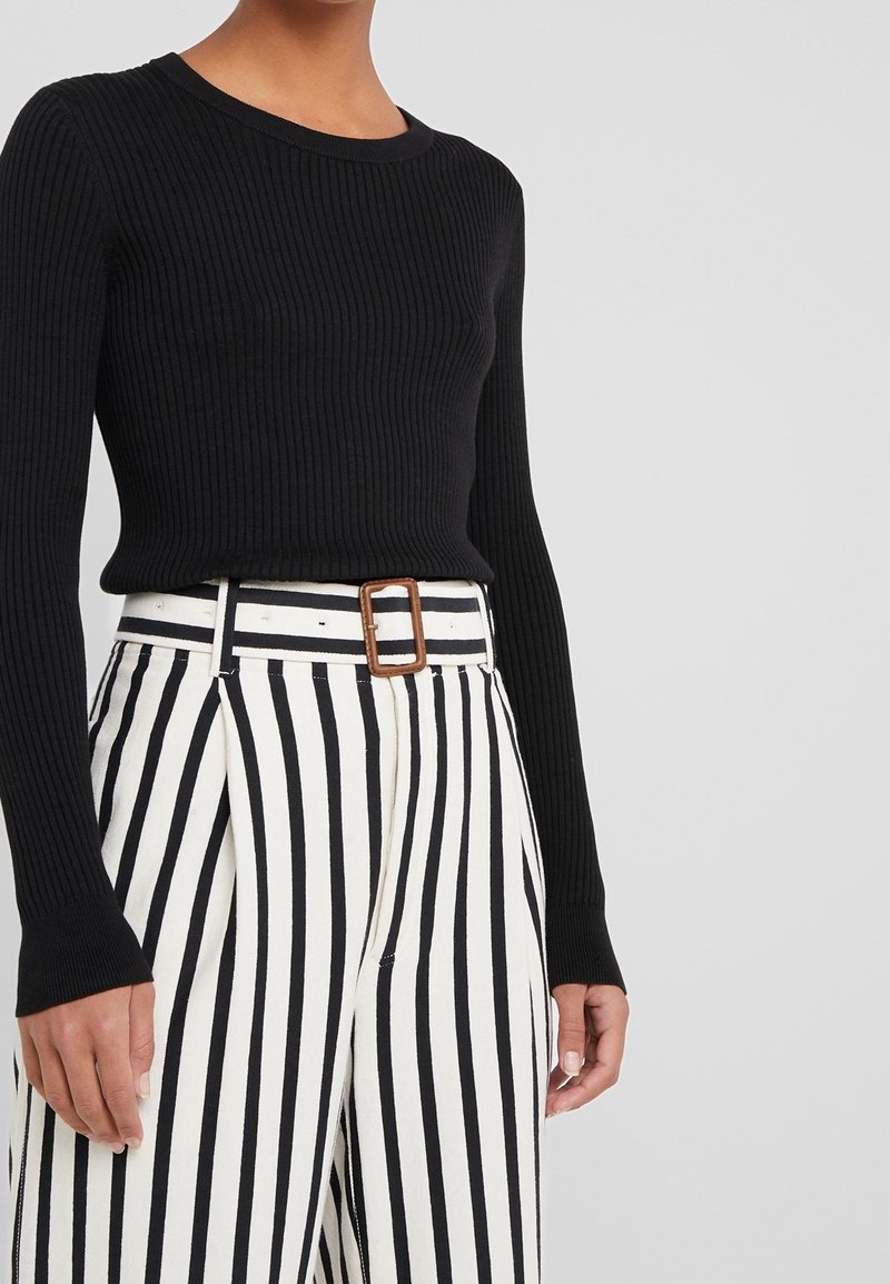 Top a maniche lunghe nero a coste abbinato a pantaloni a vita alta a righe bianche e nere, con una fibbia rettangolare marrone.