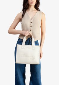 Borsa tote in pelle bianca con testo impresso "SONO UNA BORSA RESPONSABILE®", dotata di manici robusti e di una forma rettangolare strutturata.