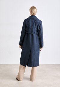 Marine trenchcoat met een ceintuur in de taille, lange mouwen en geknoopte manchetten. Kenmerkt zich door een enkele split aan de achterkant en een gladde, gestructureerde stof.