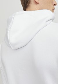 Hvit hettegenser med myk stoff, en fremtredende hette og en avslappet passform, med en jevn tekstur og minimalistisk design.