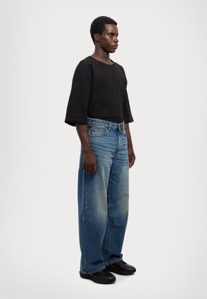 Black oversized short-sleeve shirt paired with wide-leg blue denim jeans, featuring a faded wash and subtle stitching details. Black shoes.