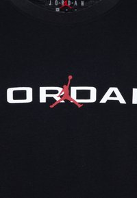 T-shirt in cotone nero con un grande testo bianco "JORDAN", evidenziato da un logo Jumpman rosso. Collo rotondo con una finitura testurizzata.