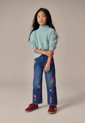 Svetlomodrý, štruktúrovaný pletený sveter; modré, široké džínsy s farebnou kvetinovou výšivkou; bordové tenisky so štruktúrovanou podrážkou.