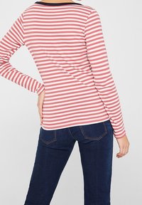 Maglietta a maniche lunghe a righe rosse e bianche con colletto blu navy, vista da dietro. Abbinata a jeans scuri. Texture liscia.