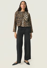 Top peplum en imprimé léopard dans des tons de marron et de noir, associé à un pantalon large taille haute noir et des ballerines noires pointues.