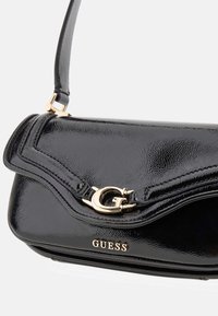 Bolso de hombro de charol negro con herrajes de logo en tono dorado y acentos de costura, que presenta un diseño de solapa estructurada.