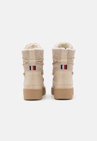 Beige vandtætte støvler med tekstureret overdel, kunstpelsforing og en tekstureret gummisål. Har tofarvede accenter i rød og blå.