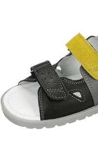 Sandal nero e grigio con una fascia gialla testurizzata, chiusure in Velcro, lati aperti e suola bianca. Presenta dettagli di cucitura.