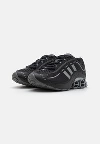 Black athletic shoes with mesh upper, textured overlays, reflective accents, and cushioned sole design featuring visible shock absorbers.