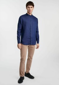 Granatowa koszula lniana z kołnierzykiem, zapinana na guziki z przodu, z długimi rękawami; połączona z beżowymi spodniami i czarnymi trampkami. Gładka tekstura i dopasowany krój.