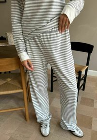Set udobne odjeće sivi i bijeli prugasti uz dugačke rukave i široke hlače. Mekana tekstura, elastična struk, uparen s bijelim tenisicama.