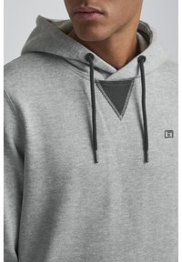 Gray hoodie made of soft fabric with a triangular black accent and front drawstrings. Features a small logo on the chest.