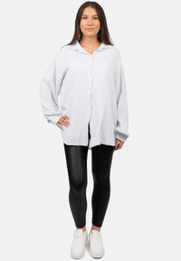 Lichtgrijs, getextureerd overhemd met kraag, gedragen over zwarte leggings en witte sneakers. Losse fit, lange mouwen met manchetten.